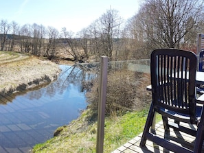 A chair overlooking a calm river with a wooden deck.