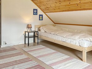 Une chambre avec un plafond en pente, un lit, une table de chevet avec une lampe et deux tableaux encadrés au mur.
