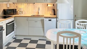 Eine kompakte Küche mit Mikrowelle, Kaffeemaschine und Geschirrspüler. Es gibt einen Esstisch mit Stühlen und einen Schachbrettboden.