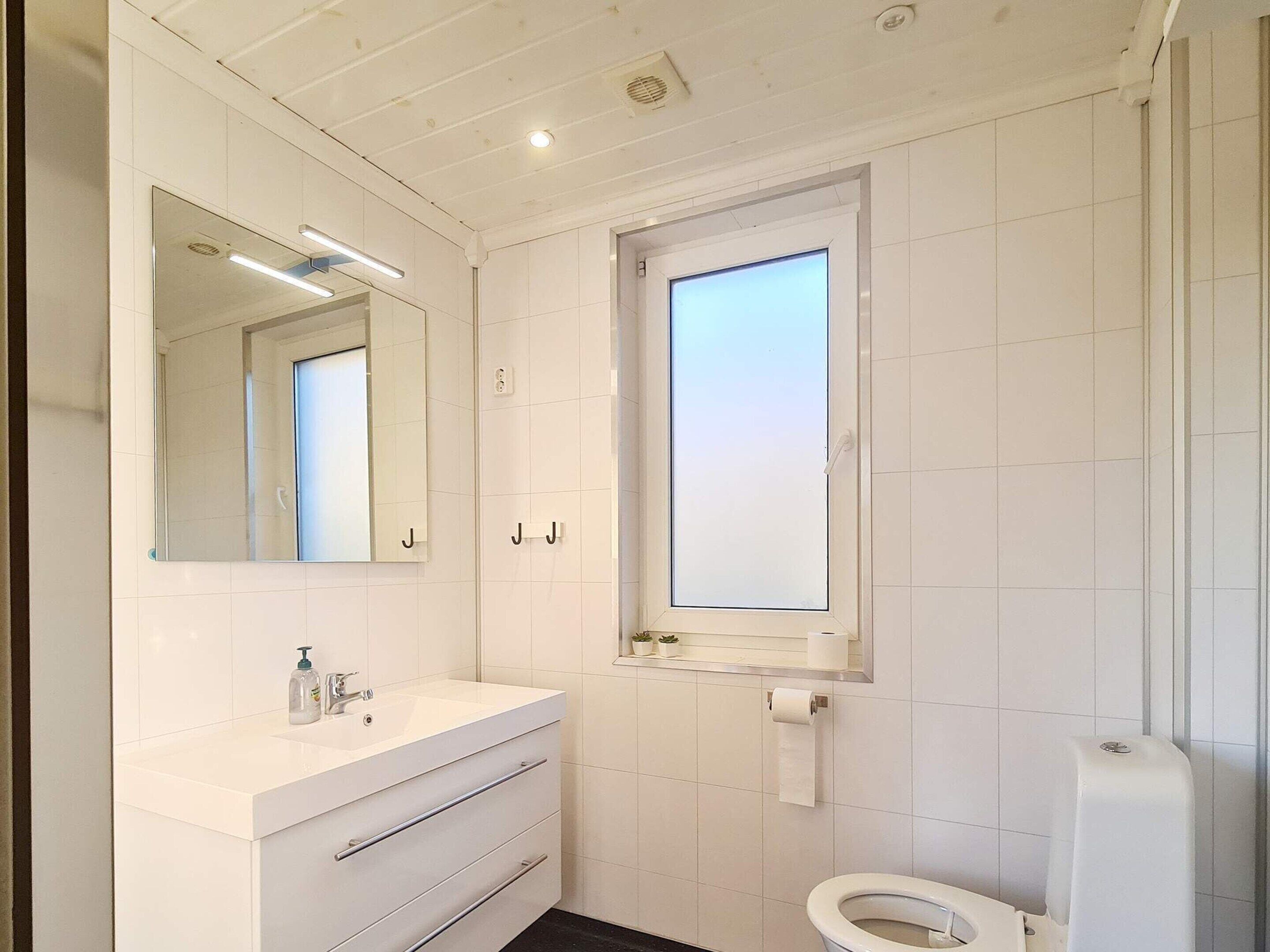 Ett modernt badrum med ett vitt handfat, en spegel, ett fönster och en toalett.