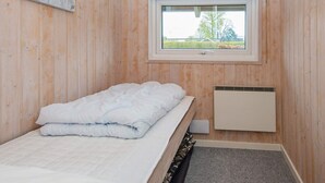 Une chambre avec un lit simple, une fenêtre, un radiateur et des murs en bois.