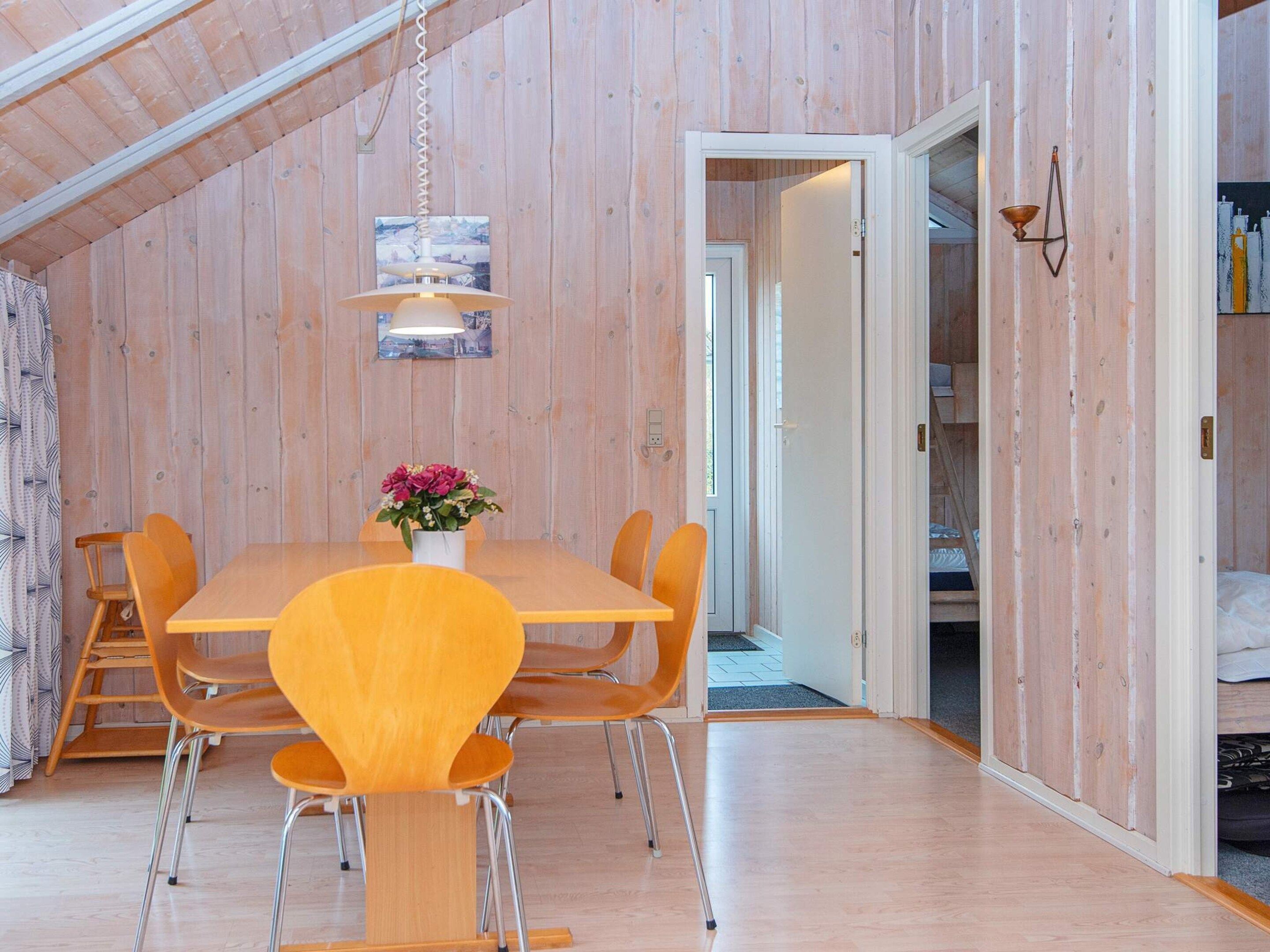 A dining area with a wooden table and chairs, a hanging light fixture, and a door leading to another room.