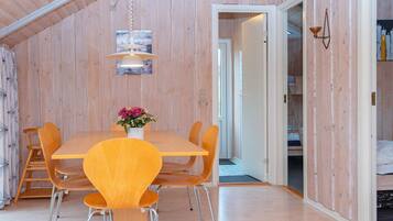 Un comedor con una mesa y sillas de madera, una lámpara colgante y una puerta que da a otra habitación.