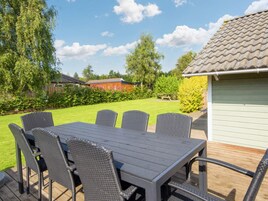 An outdoor patio with a table and chairs, surrounded by a lawn and a building with a tiled roof.