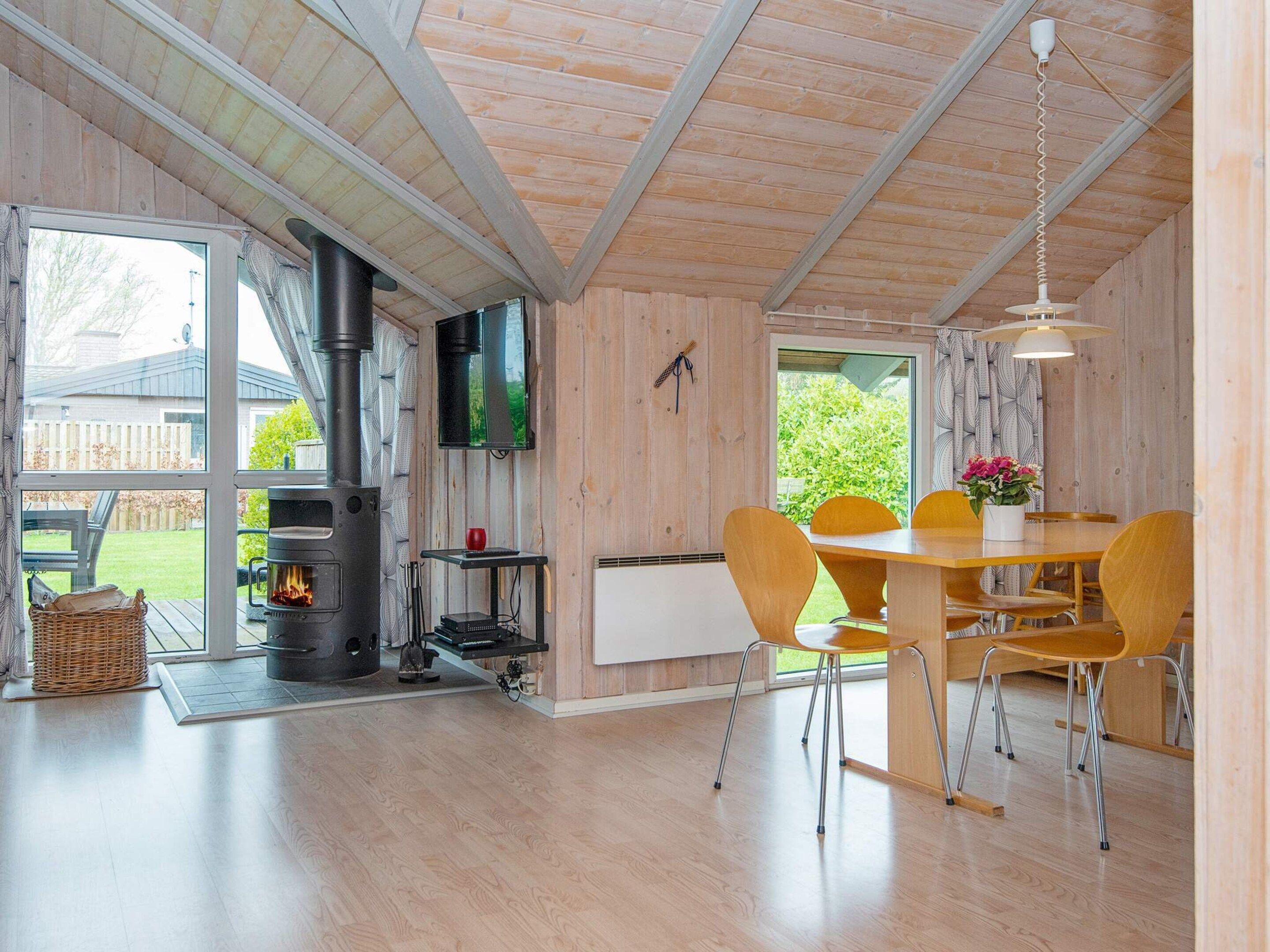 A cozy room with a wooden interior, a fireplace, a dining table with chairs, and a large window.