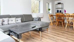 A modern living room with a grey sofa, a wooden coffee table, and a dining area with wooden chairs and a table. - 5 Person Holiday Home in Borkop (Borkop)