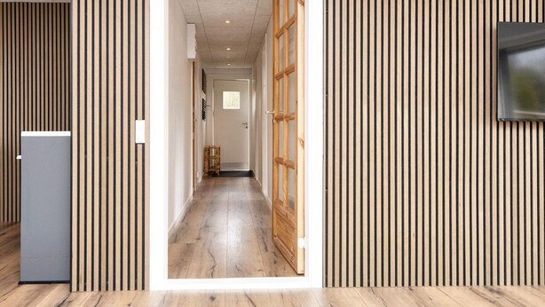 A hallway with wooden paneling, a door at the end, and a television mounted on the wall. - 5 Person Holiday Home in Borkop (Borkop)