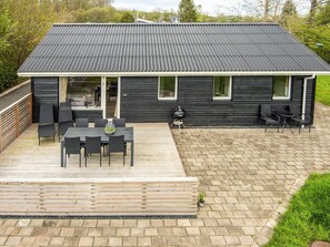 Une maison moderne à l’extérieur sombre, dotée d’un patio couvert avec une table et des chaises, ainsi que d’un barbecue.
