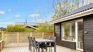A wooden deck with a table and chairs, a sliding glass door, and a view of a house in the background. - 5 Person Holiday Home in Borkop (Borkop)