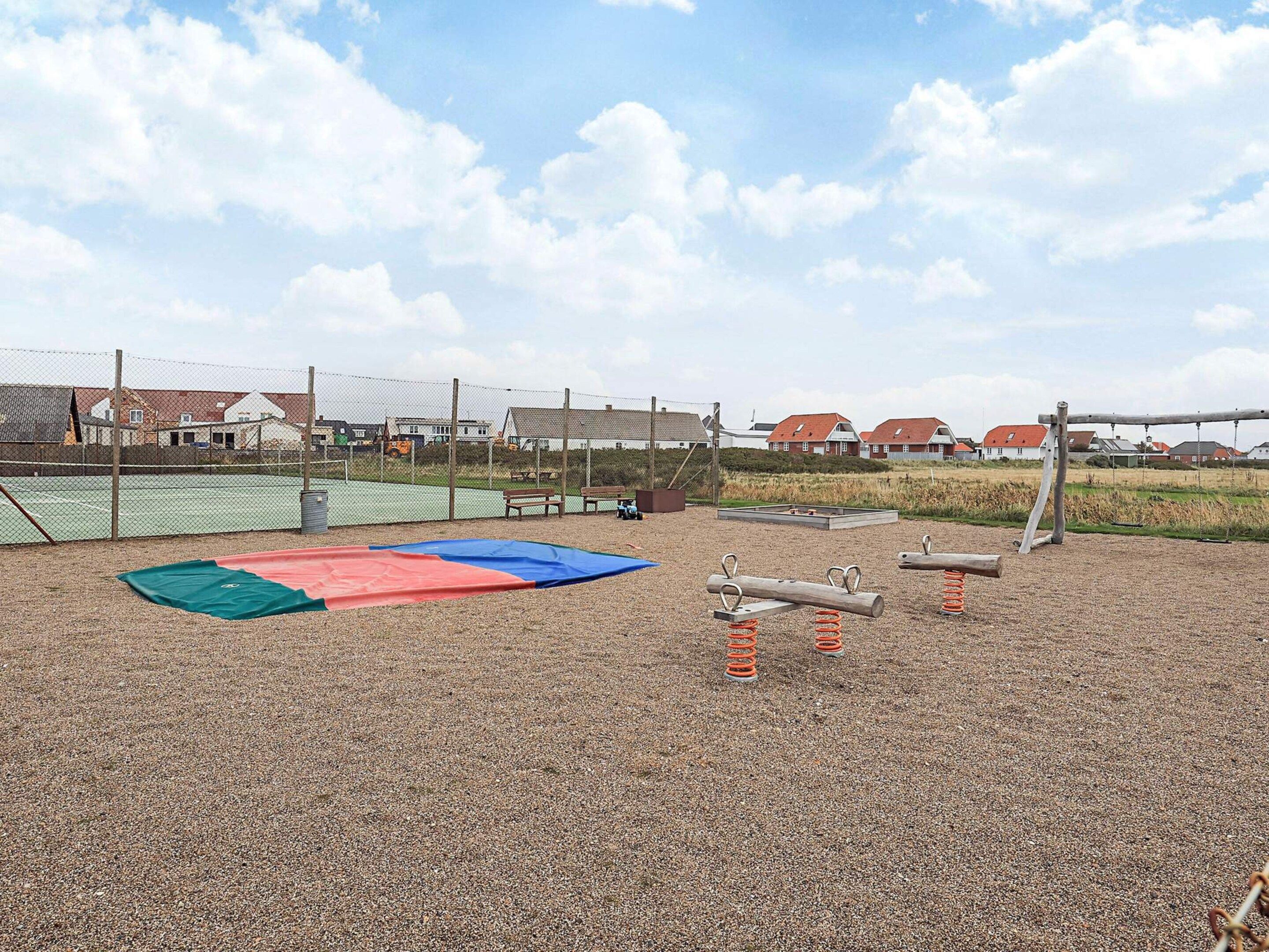 Une aire de jeux avec un terrain de tennis entouré de filets, des balançoires et une bascule.