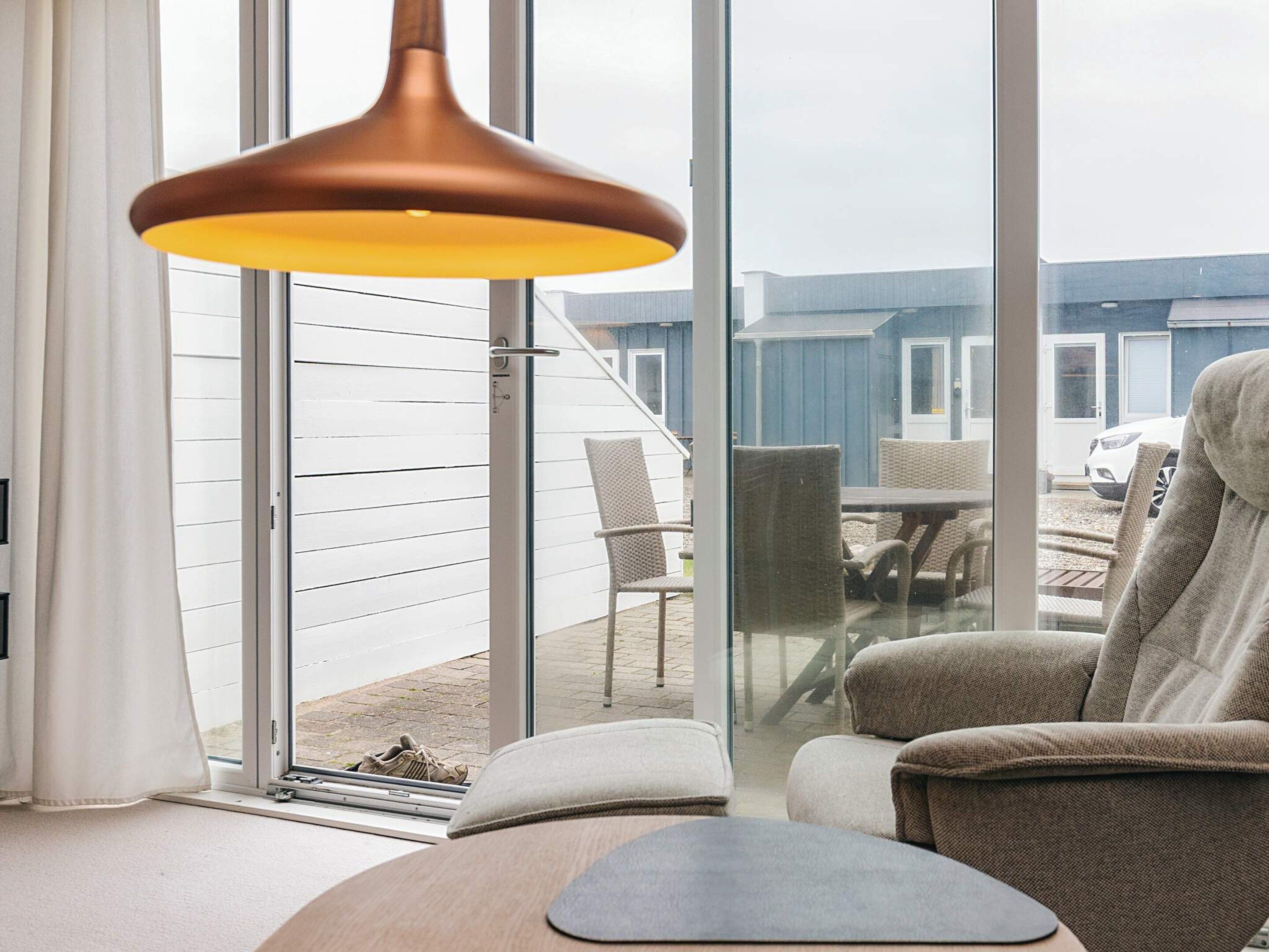 A modern living room with a large window, a sofa, a chair, and a hanging light fixture.