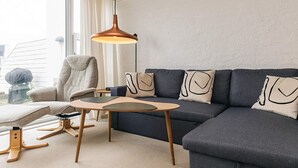 Una sala moderna con un sofá gris oscuro, una mesa de centro de madera, un sillón color beige y una lámpara de pie.