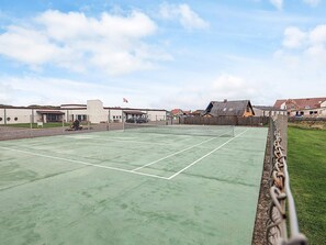 An outdoor tennis court with a chain-link fence, surrounded by residential buildings and a grassy area. - 4 Person Holiday Home in Vestervig (Vestervig)