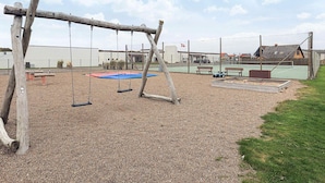Un parque infantil con columpios, un trampolín y una cancha de tenis vallada.