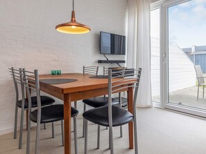 Zona pranzo con tavolo in legno e sei sedie, una lampada a sospensione, una televisione a schermo piatto montata a parete e una porta scorrevole in vetro che dà su un patio esterno.