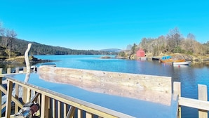 A wooden dock extending into a calm lake with boats docked nearby and a red building in the background.