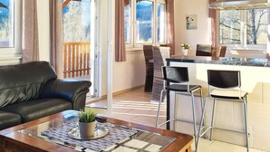 A modern kitchen with a bar area, a dining table with chairs, and a sofa in a living area with a view of the outdoors.