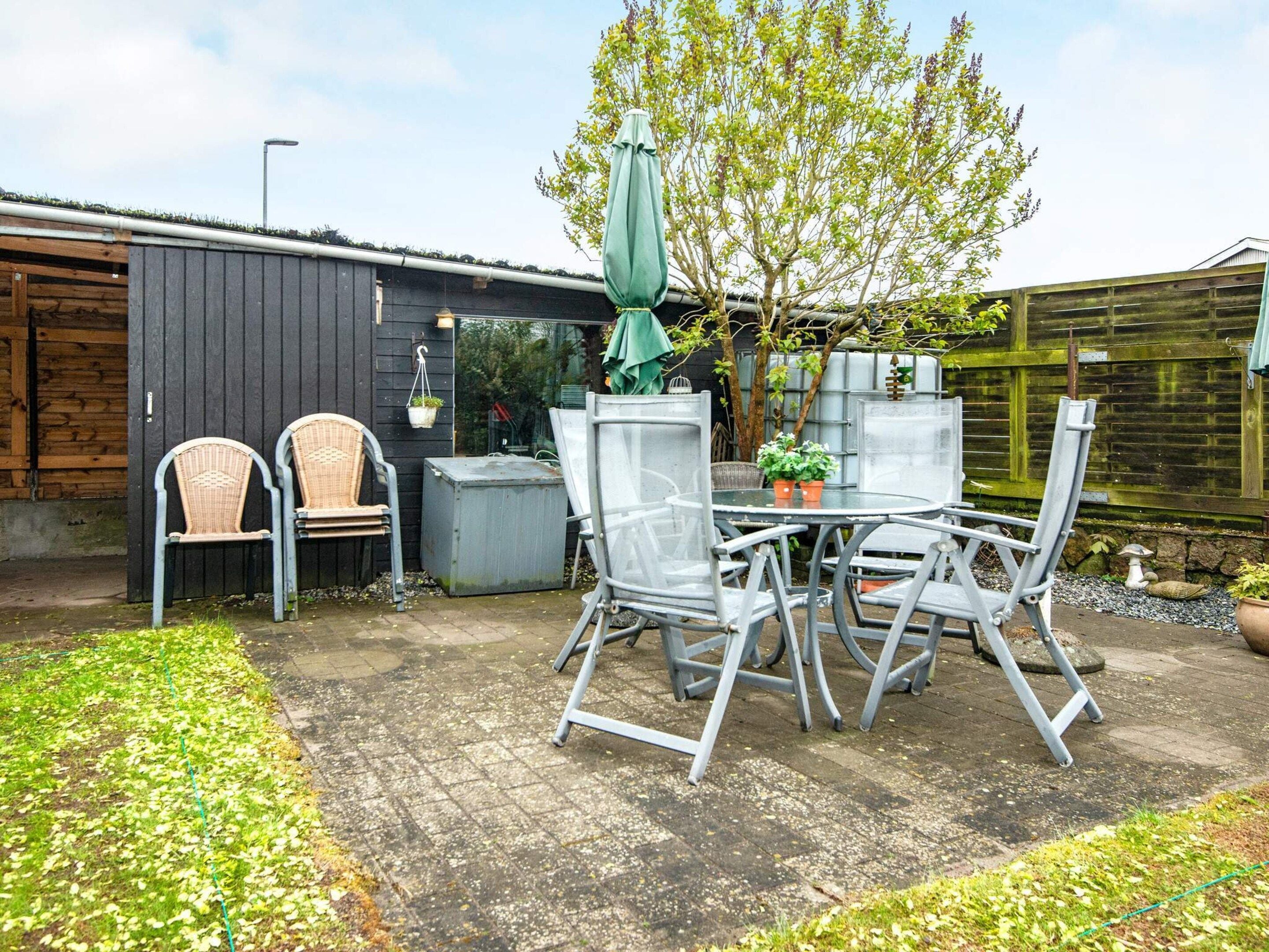 En udendørs terrasse med et bord og stole, omgivet af et træhegn og en have.