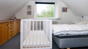 A bedroom with a crib, a bed, a dresser, a window, and a radiator. - 6 Person Holiday Home in Skaerbaek-by Traum (Skaerbaek)