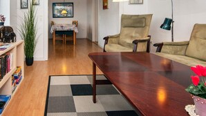 A living room with a wooden coffee table, a beige armchair, and a sofa. There is a dining table with chairs in the background. - 6 Person Holiday Home in Skaerbaek-by Traum (Skaerbaek)