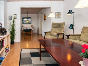 A living room with a wooden coffee table, a beige armchair, and a sofa. There is a dining table with chairs in the background. - 6 Person Holiday Home in Skaerbaek-by Traum (Skaerbaek)