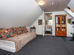 A cozy attic bedroom with a bed, a colorful pillow, a small table, a wooden bookcase, and a door leading to another room.