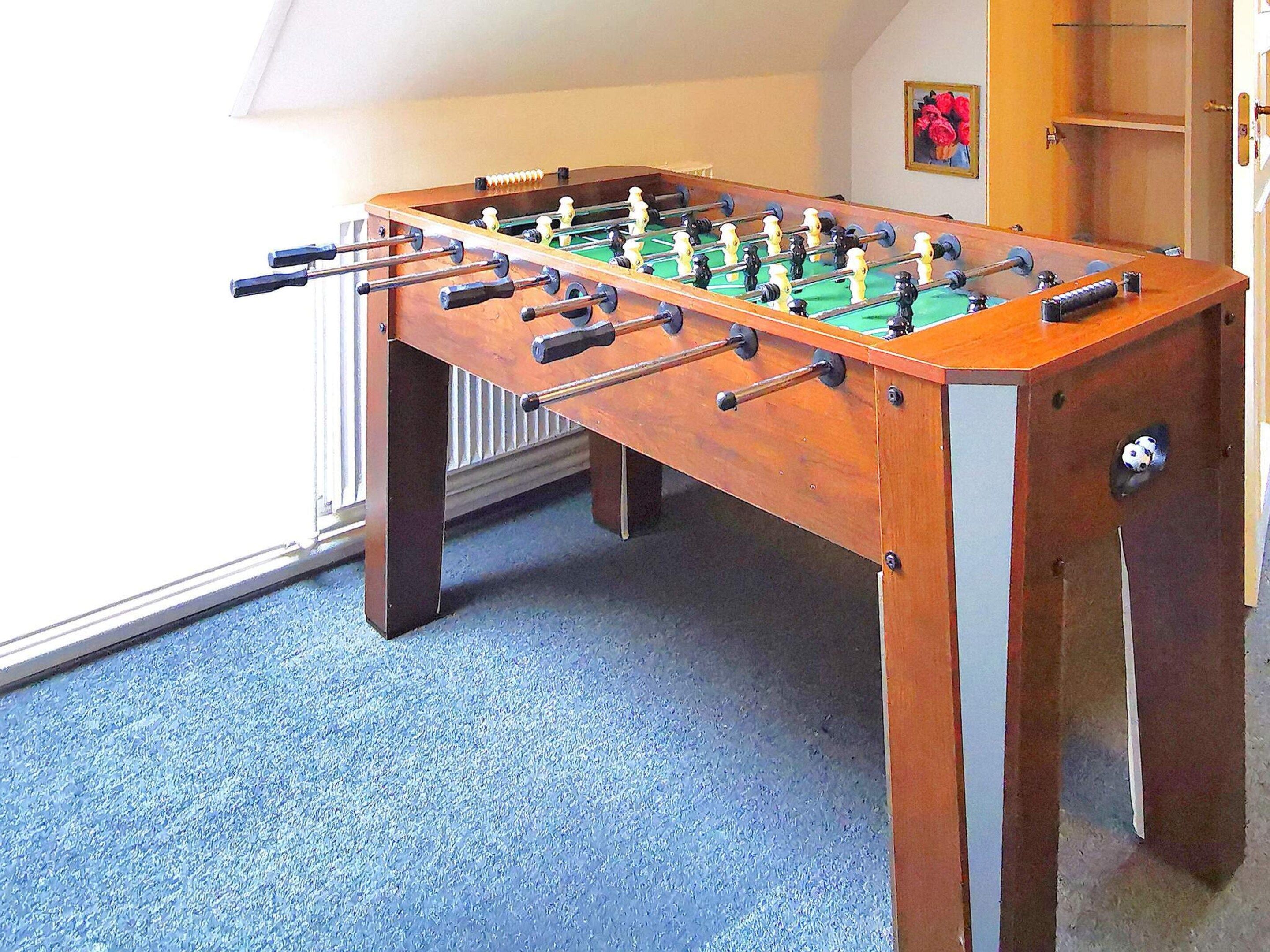 A foosball table in a room with a blue carpet and a radiator.