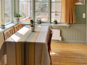 A dining area with a table set for two, a window with curtains, and potted plants on the windowsill.