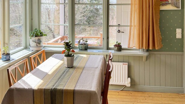Un coin repas avec une table dressée pour deux personnes, une fenêtre avec des rideaux et des plantes en pot sur le rebord de la fenêtre.