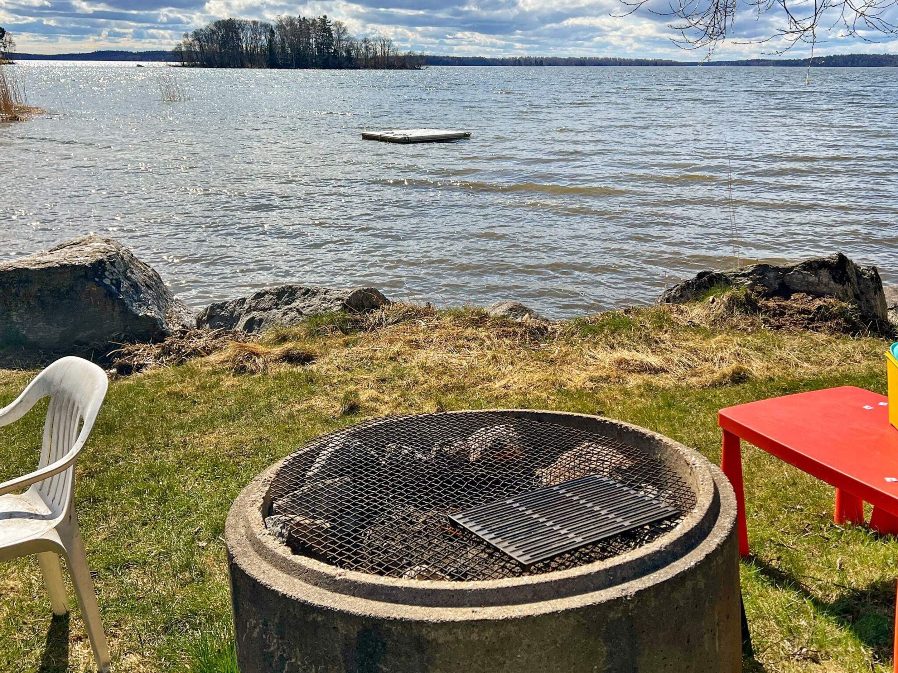 A lakeside outdoor seating area with a grill, a red table, and a white chair.