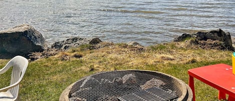 A lakeside outdoor seating area with a grill, a red table, and a white chair.
