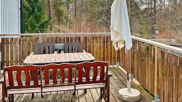 A wooden deck with a table and chairs, a bench, and a white umbrella.