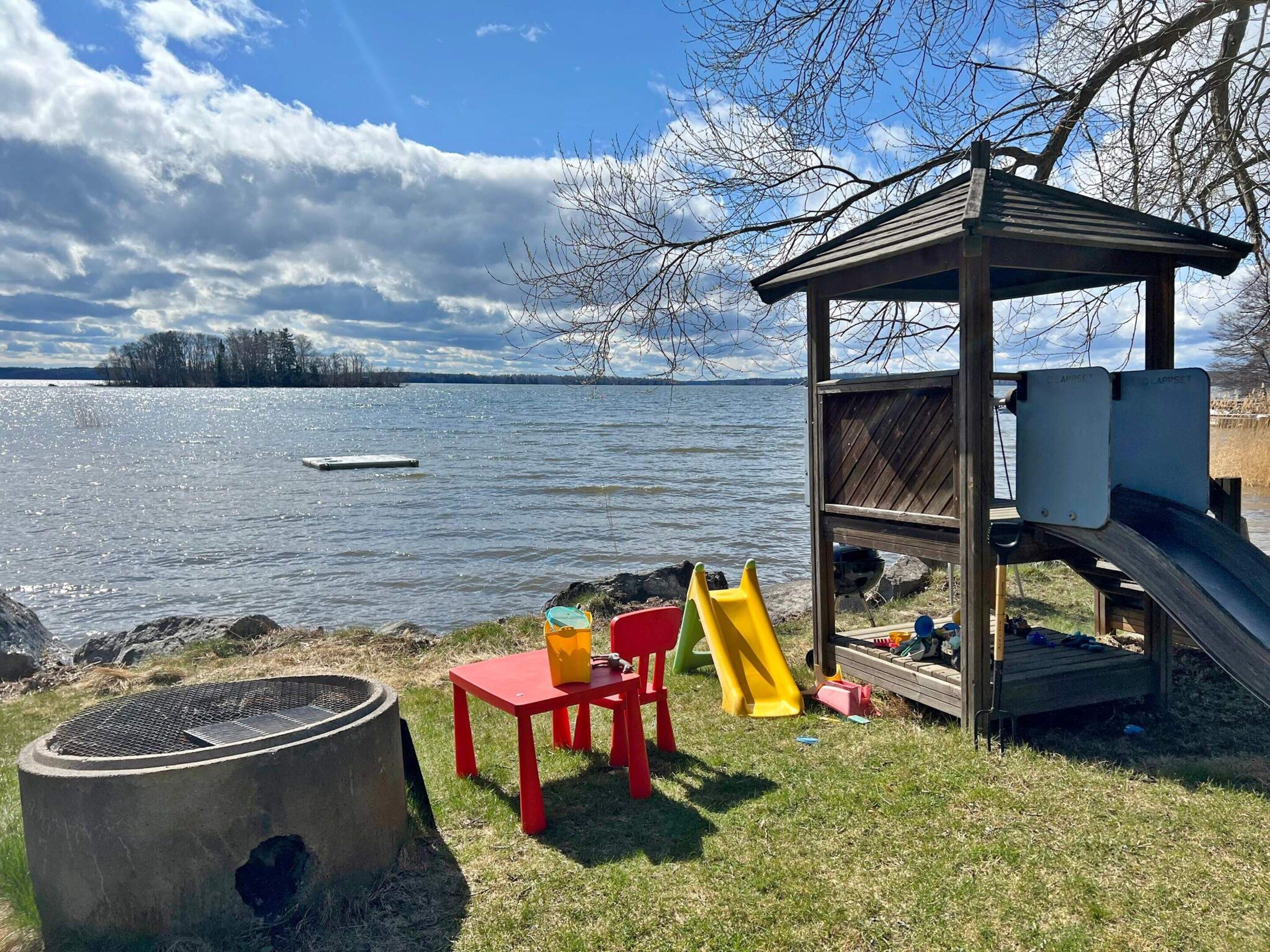 Un parque infantil junto al lago con tobogán, una fogata y una mesa de picnic.