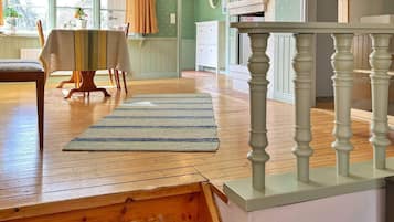 Una habitación con piso de madera, un tapete a rayas, una mesa de comedor con sillas y una escalera con barandilla blanca.