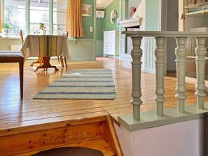 A room with a wooden floor, a striped rug, a dining table with chairs, and a staircase with a white balustrade. - 6 Person Holiday Home in Munso (Munsö)