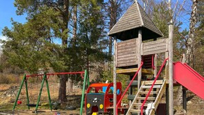 Une aire de jeux avec des balançoires, un toboggan et une structure d’escalade.