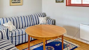 Un canapé à rayures avec des coussins à motifs floraux, une table ronde en bois et un tapis bleu à motifs floraux dans une pièce dotée d’un plancher en bois et d’un radiateur blanc.