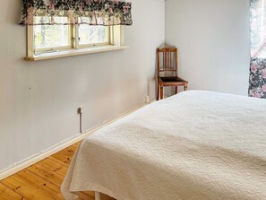 A bedroom with a bed, a window with floral curtains, a wooden chair, and a plain wall. - 6 Person Holiday Home in Munso (Munsö)