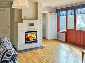A room with a fireplace, a wooden floor, a striped sofa, and a window with a red door. - 6 Person Holiday Home in Munso (Munsö)