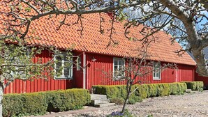 Una casa de madera roja con techo de tejas, un camino de piedra y setos bien cuidados.