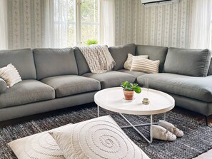 A modern living room with a grey sectional sofa, a round coffee table with a potted plant, and decorative pillows. - 8 Person Holiday Home in Hestra (Hestra)