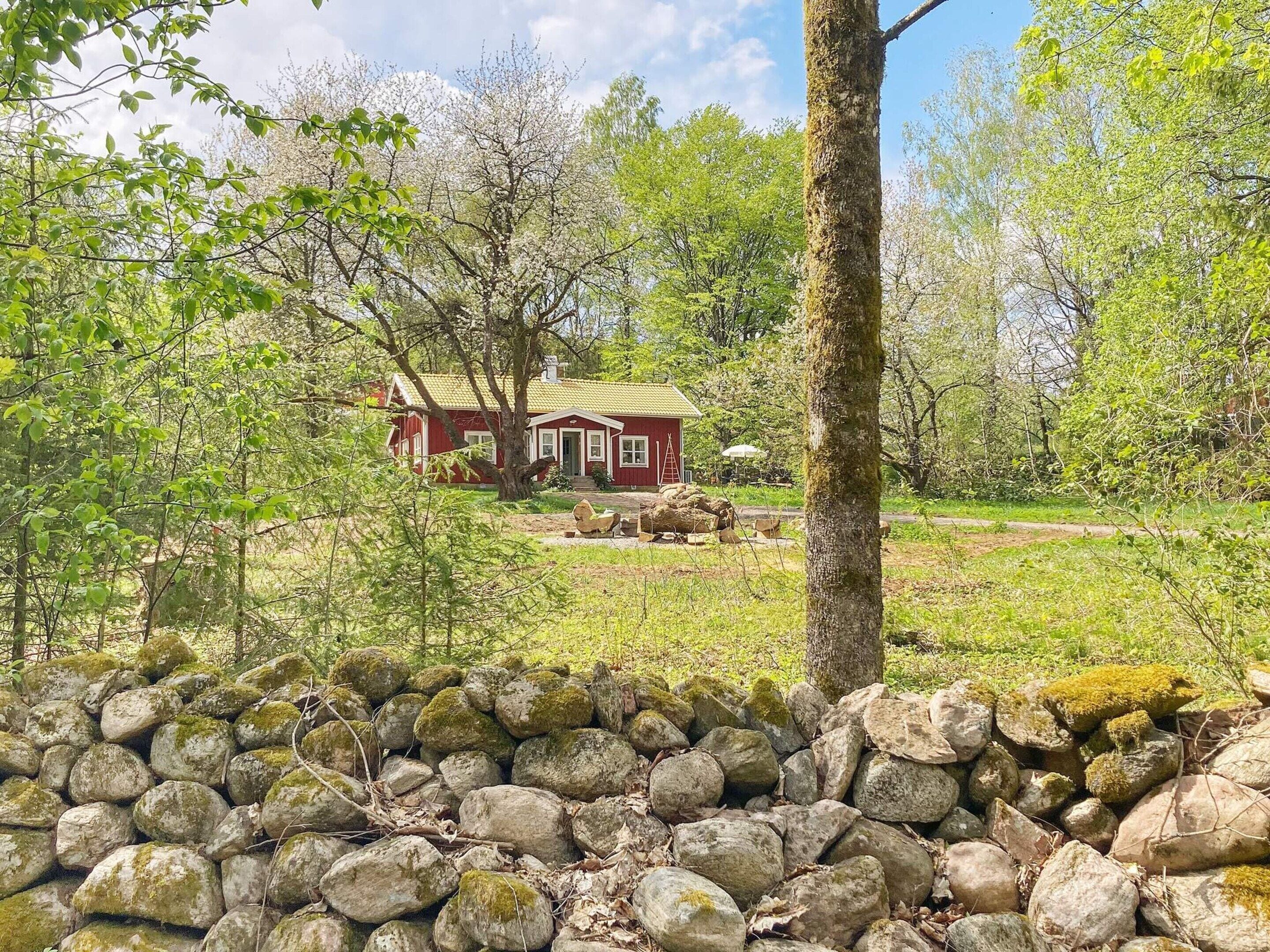 A red house with a green roof, surrounded by trees and a stone wall.