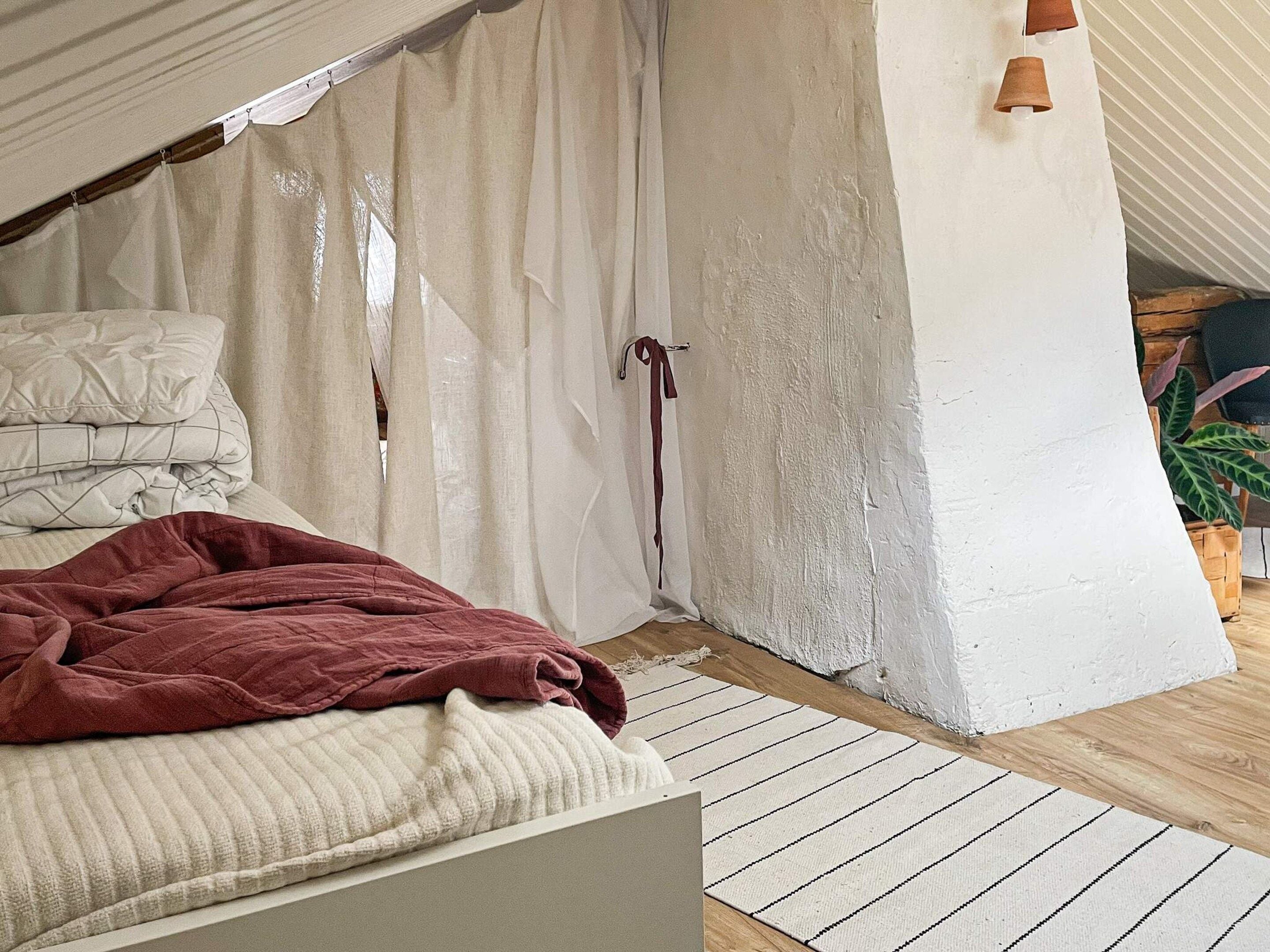 Un dormitorio con una cama, una lámpara colgante, una cortina y una planta.