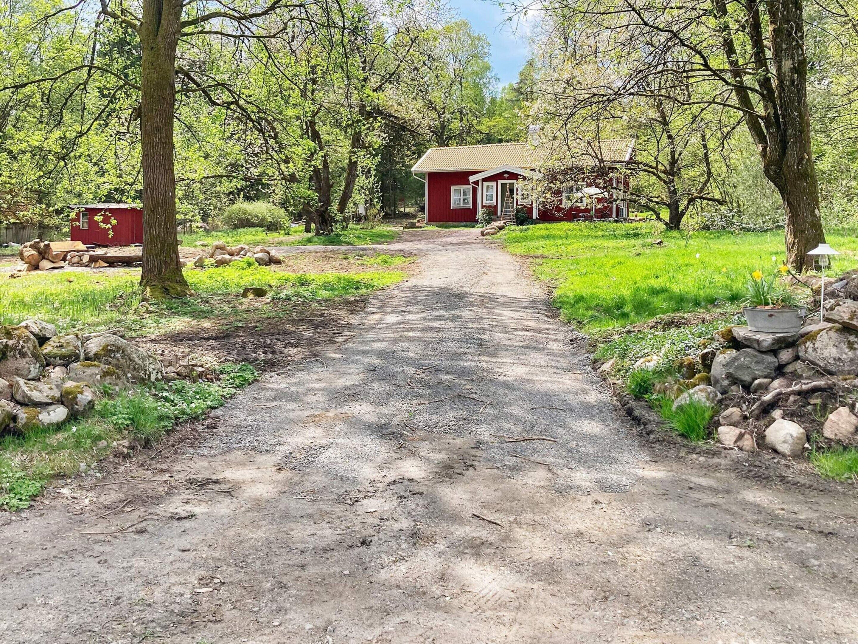 A rural pathway leading to a red house surrounded by trees and greenery.