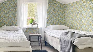 Un dormitorio con dos camas, una ventana con vista a vegetación, un escritorio con lámpara y una pared con diseño.