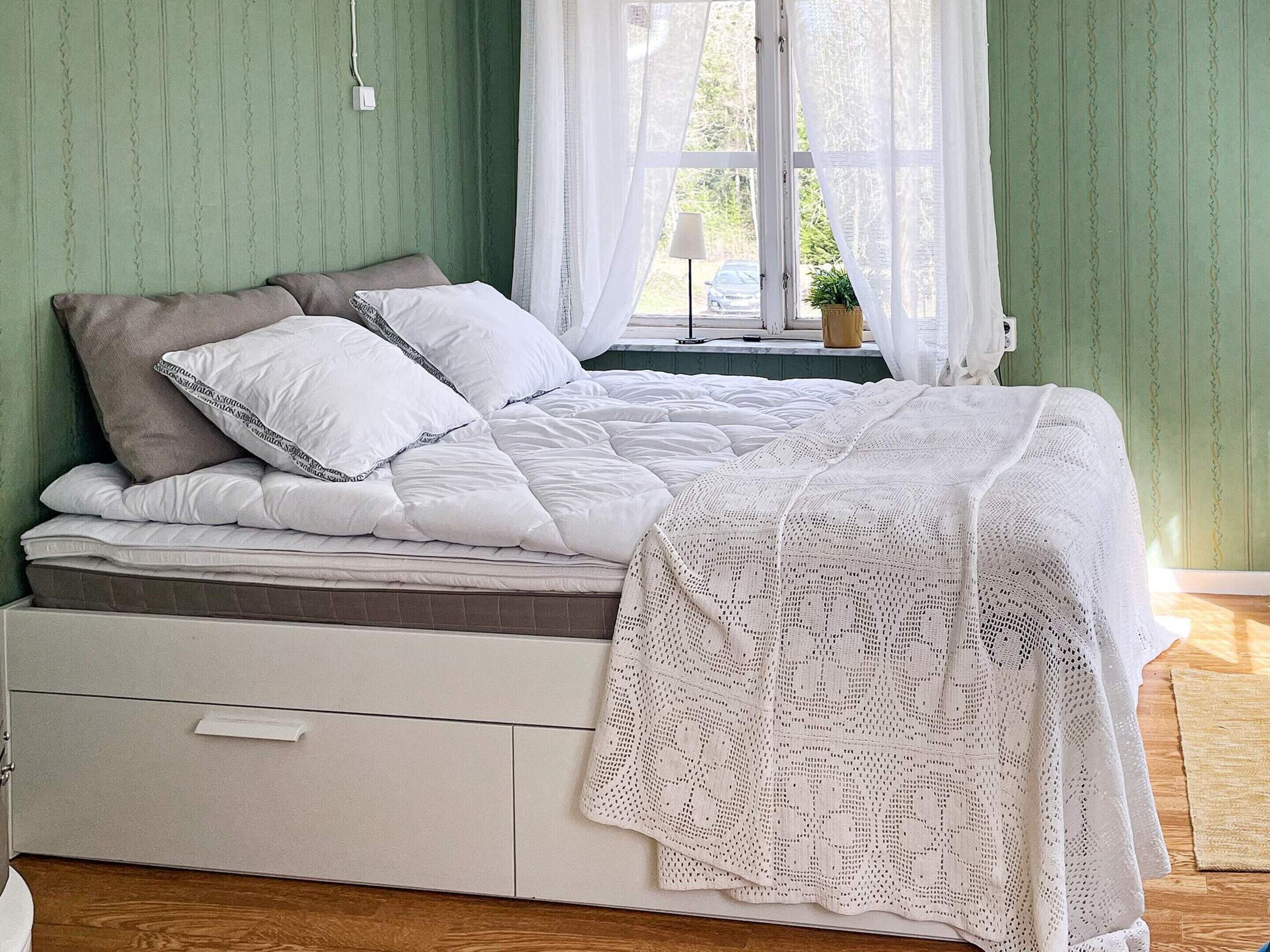A bedroom with a bed, a bedside table, a lamp, and a window with curtains.