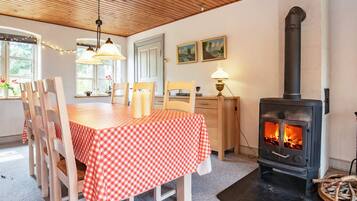 Un comedor con mantel a cuadros, sillas de madera, una lámpara de mesa y un estufa de leña.