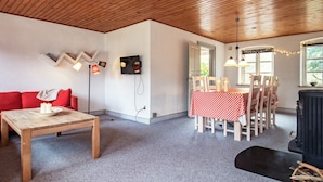 A cozy room with a wooden ceiling, a red sofa, a dining table with chairs, a fireplace, and a TV mounted on the wall. - 6 Person Holiday Home in Aeroskobing (Aeroskobing)