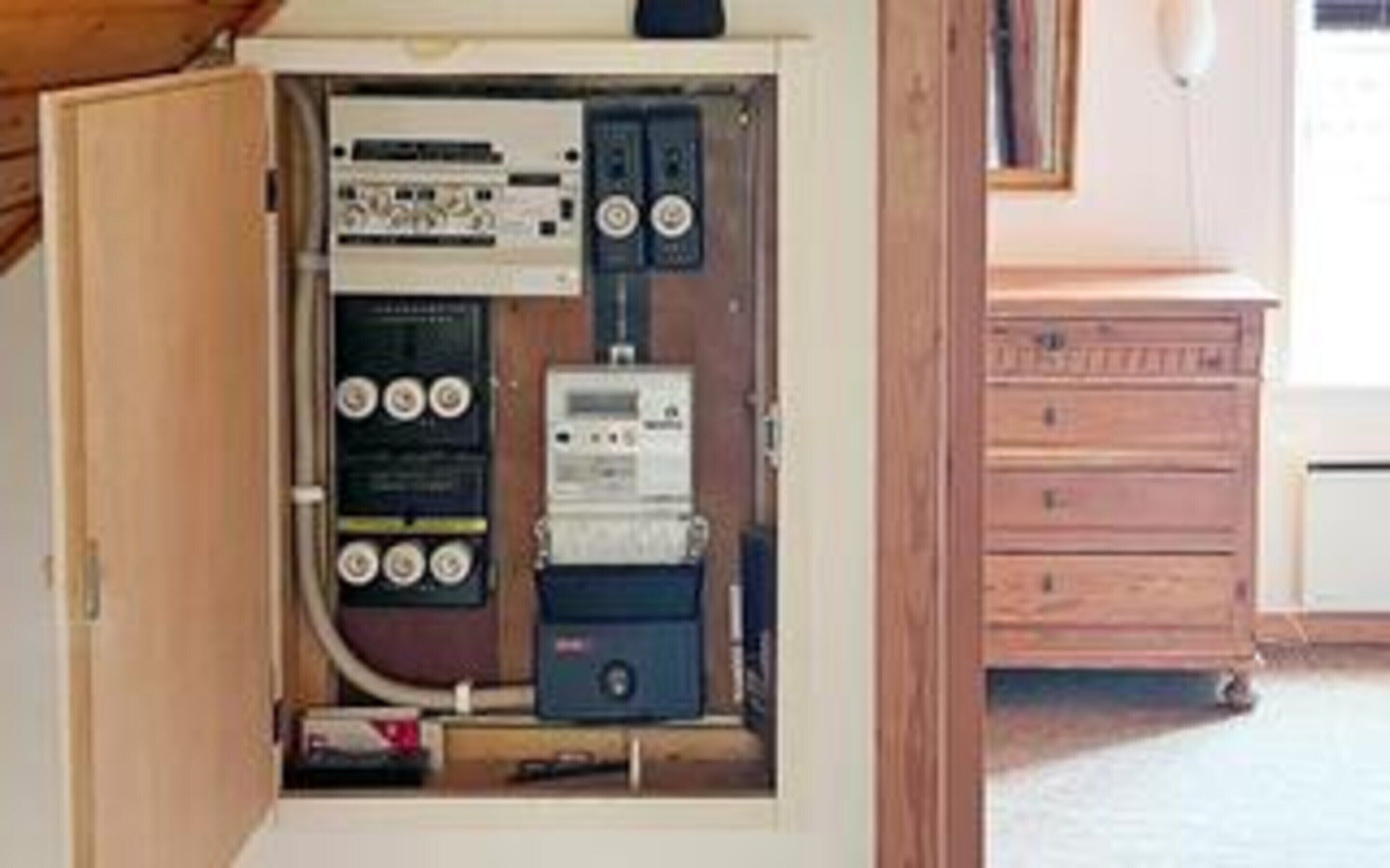 An electrical panel with various switches and meters, a wooden cabinet, and a white appliance in the background.
