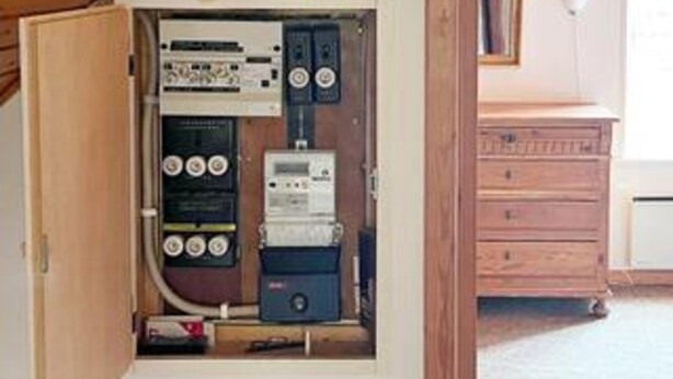 An electrical panel with various switches and meters, a wooden cabinet, and a white appliance in the background. - 6 Person Holiday Home in Aeroskobing (Aeroskobing)